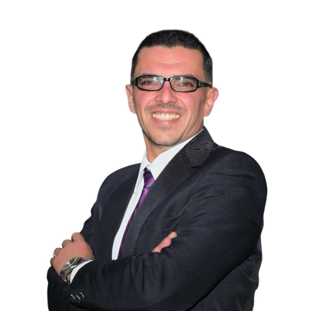 Smiling man in a dark suit with a purple tie and glasses, arms crossed.