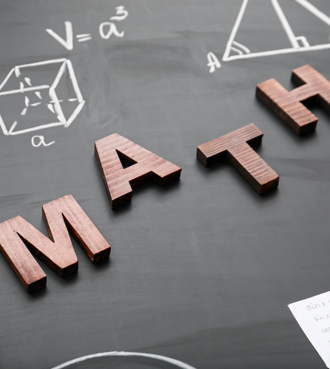 Wooden letters spelling MATH on a chalkboard with chalk diagrams of a cube and a triangle.